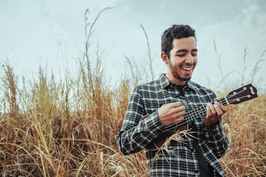 man playing ukulele while standing on grass field