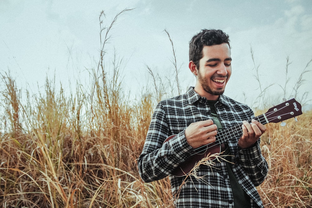 man playing ukulele while standing on grass field