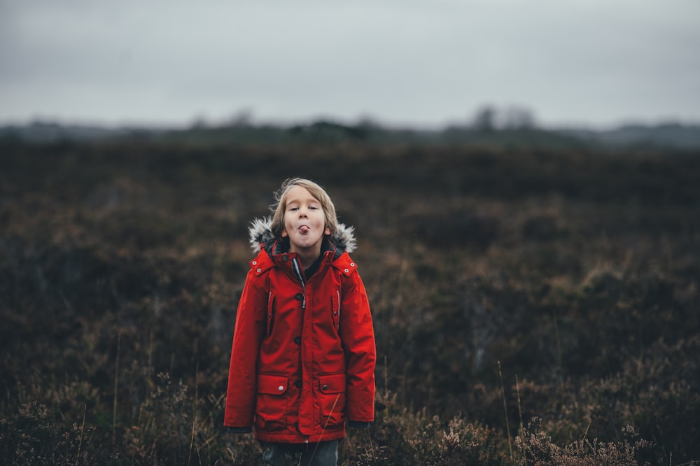 child showing tongue while standing on grass field during daytime