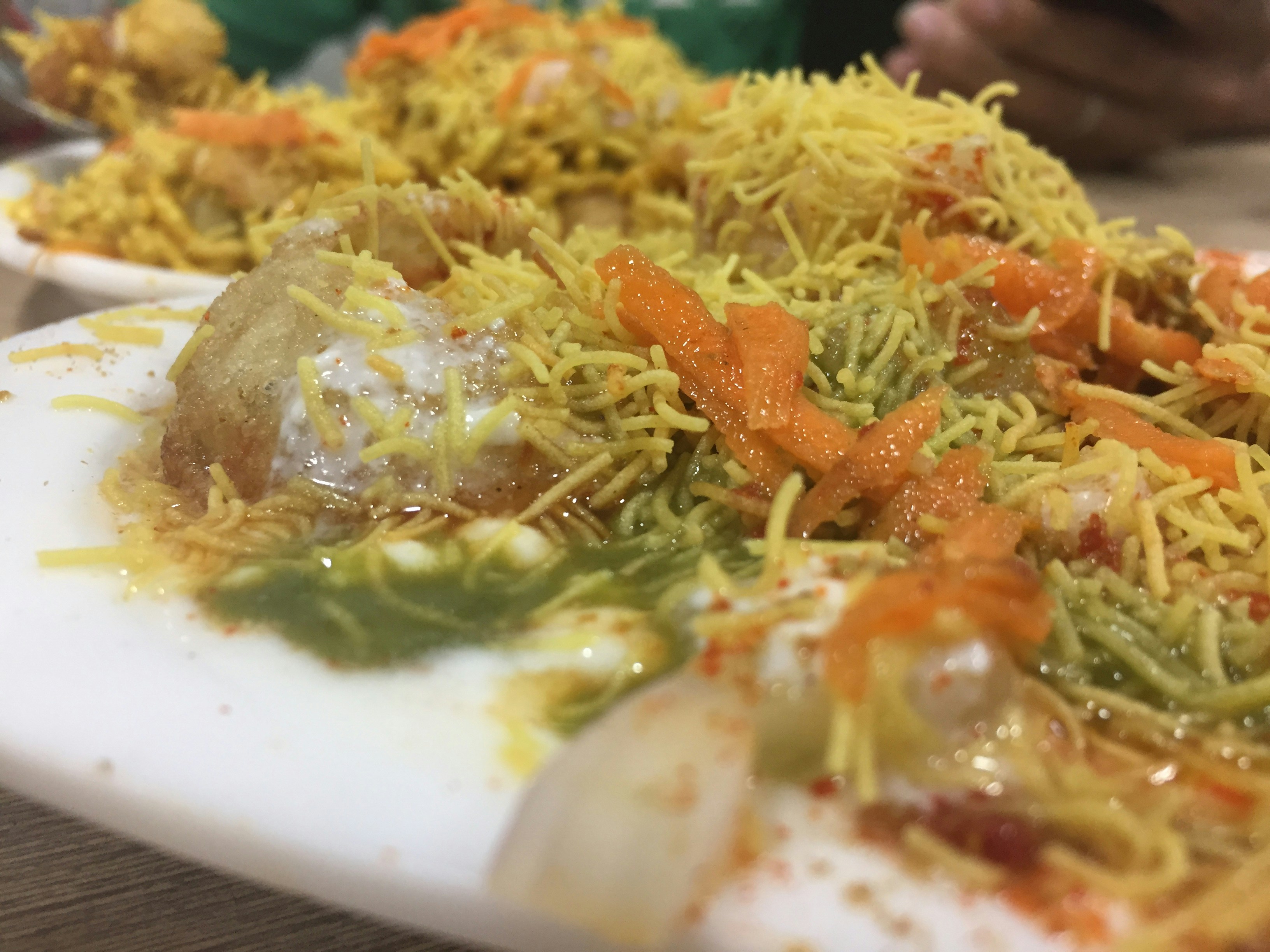 Steaming bowl of soft yellow locho garnished with chutney and sev, dark wooden table, warm amber food stall light