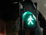 A pedestrian traffic light glowing green, featuring an illuminated walking figure, indicating it's safe for pedestrians to cross. The background is dark, suggesting nighttime or an indoor environment.
