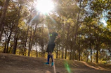 Athlete wearing Caserne sunglasses while running through a sunlit forest path.