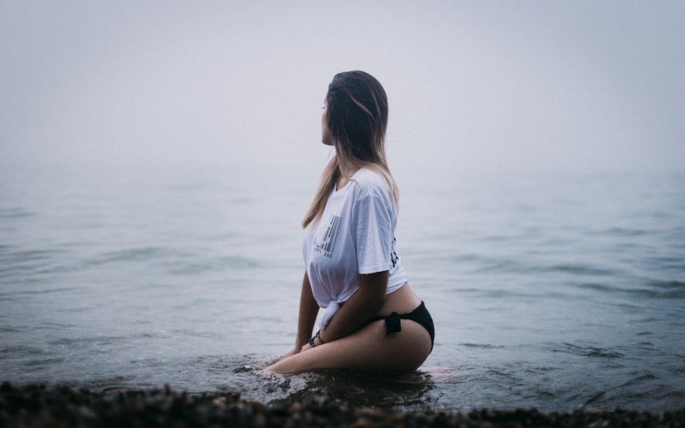 Frau sitzt auf schwarzer Oberfläche und schaut auf Gewässer