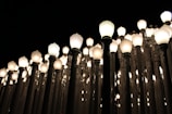 An array of vintage street lamps densely arranged, each with a glowing bulb, creating a pattern of light against a dark night sky.