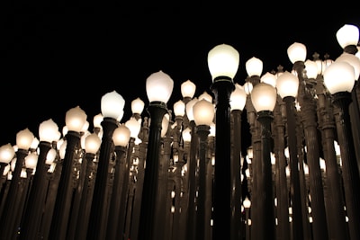 An array of vintage street lamps densely arranged, each with a glowing bulb, creating a pattern of light against a dark night sky.