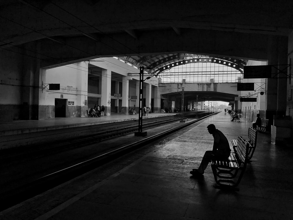 silhueta do homem sentado no banco ao lado do trilho do trem