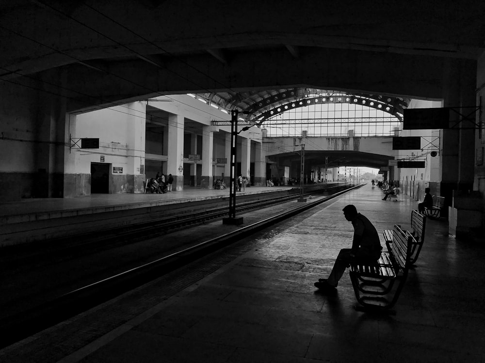 silhouette d’homme assis sur un banc à côté du rail de train