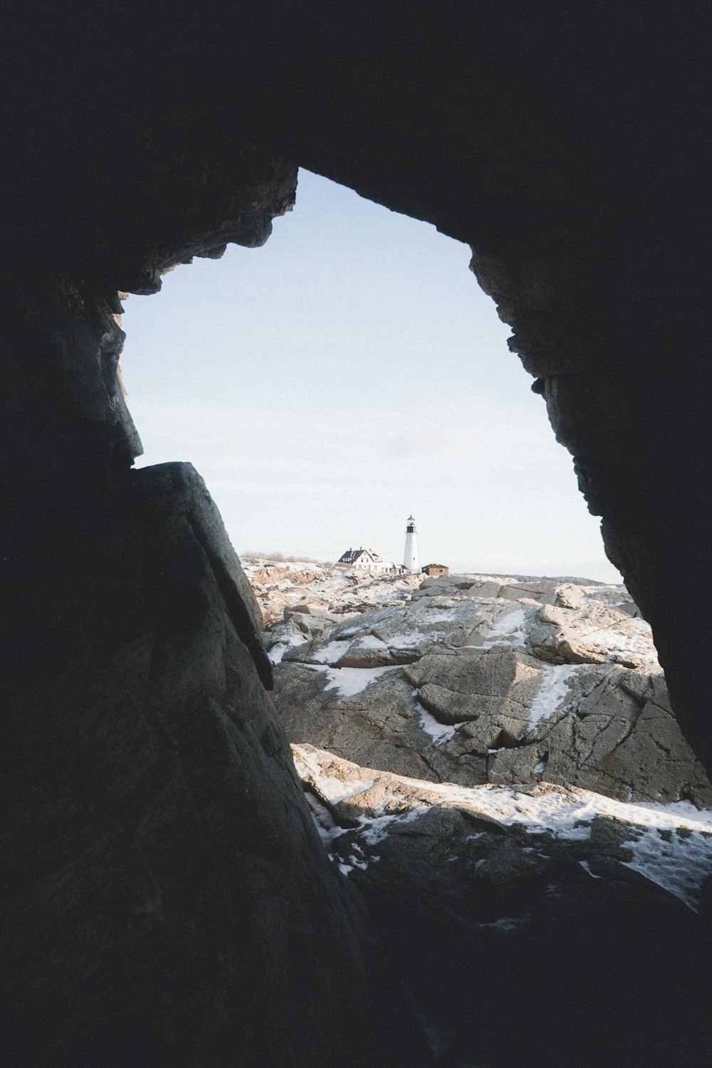 Vista della grotta dell'isola di pietra con il faro e la casa in lontananza durante il giorno