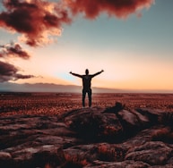 person standing on rock raising both hands