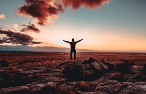 person standing on rock raising both hands