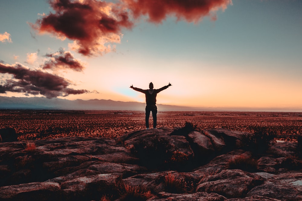 person standing on rock raising both hands