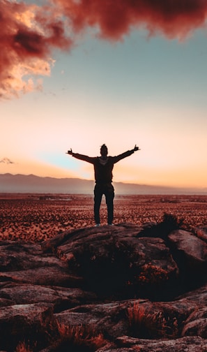 person standing on rock raising both hands