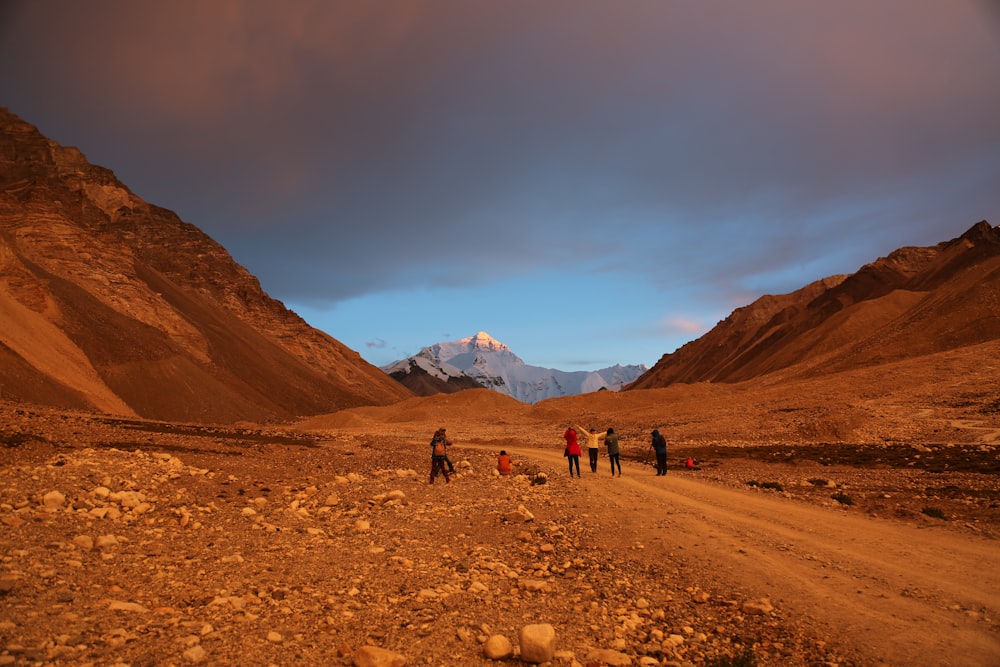 group of people walks on dirt road leading to mountain