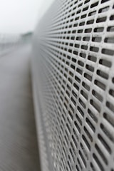 A close-up view of a perforated metal surface with an array of evenly spaced rectangular holes, creating a sense of depth as the focus diminishes in the background. The surface stretches diagonally across the image, highlighting its linear pattern.