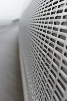 A close-up view of a perforated metal surface with an array of evenly spaced rectangular holes, creating a sense of depth as the focus diminishes in the background. The surface stretches diagonally across the image, highlighting its linear pattern.