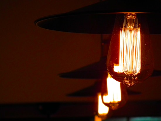 A series of vintage-style filament light bulbs emit a warm, soft glow in a dimly lit environment. The bulbs are encased in transparent glass and are hanging from dark, metallic fixtures. Their arrangement suggests a cozy and intimate atmosphere.