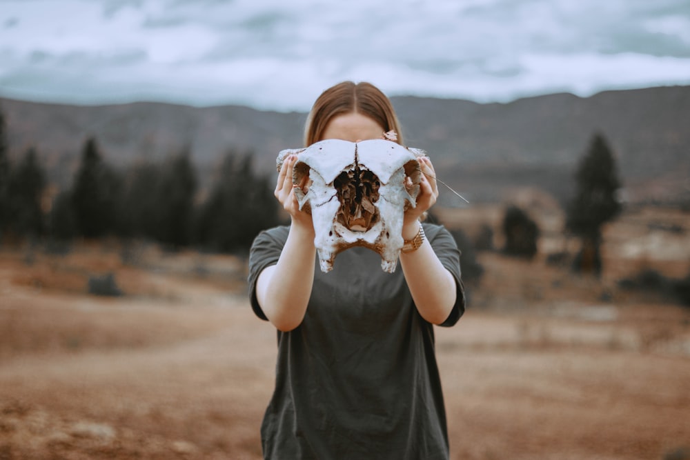 person holding white skull standing on brown sands