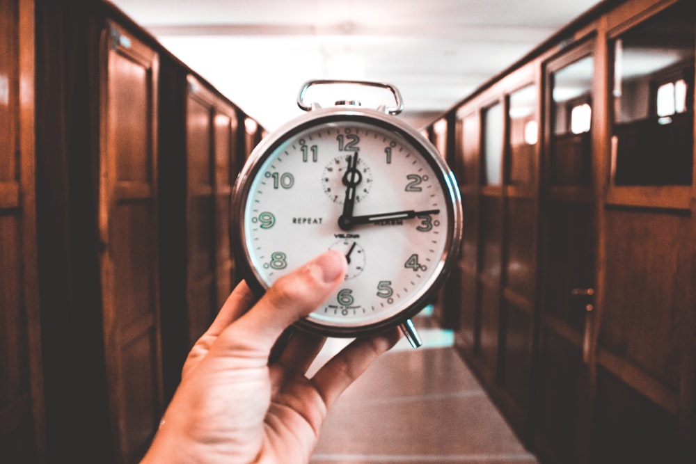 person holding dual bell alarm clock reading at 12:14 o' clock