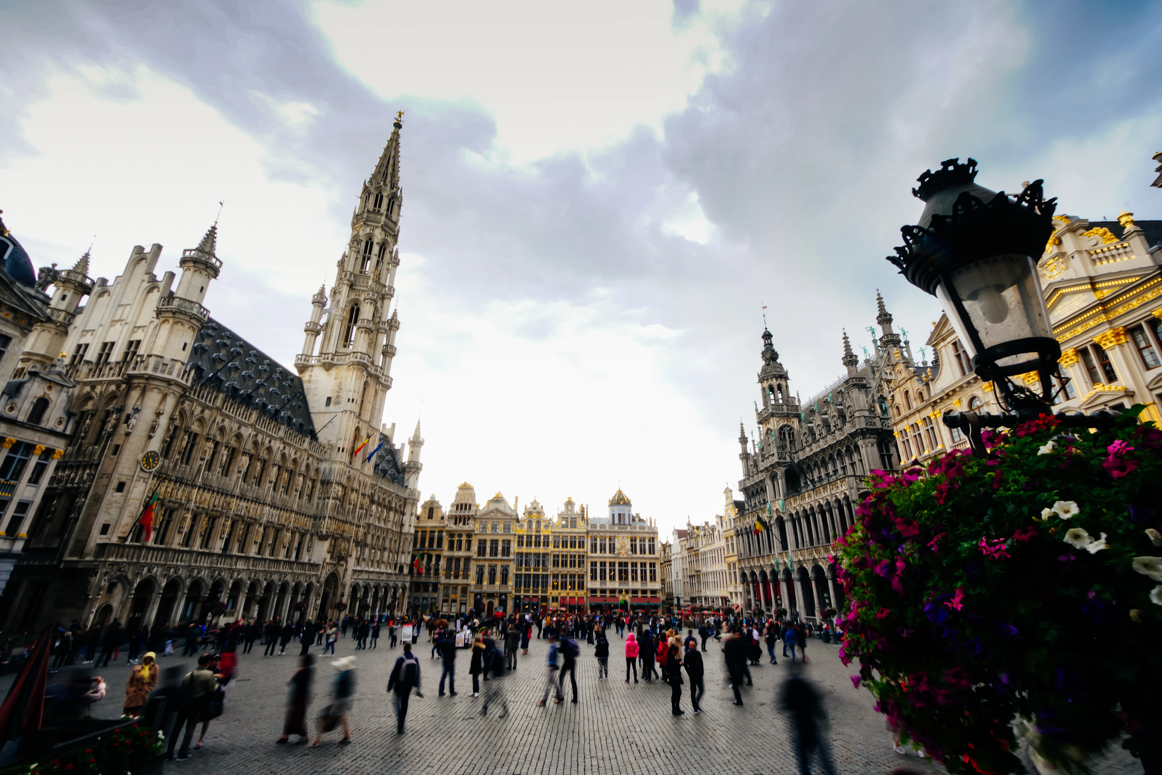 Crowds crossing the Grand-Place in Brussels, ringed by gilded baroque guild houses beneath the Gothic spire of the Town Hall
