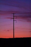 High voltage power lines glowing against a twilight sky with colorful background