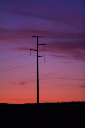 High voltage power lines glowing against a twilight sky with colorful background