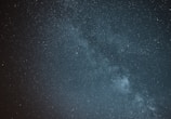 A vast night sky filled with countless stars, with the Milky Way galaxy clearly visible as a bright, cloudy band stretching across the center. The image conveys a sense of depth and the infinite expanse of the universe.