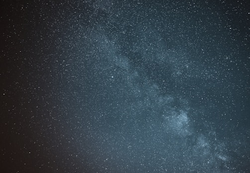 A vast night sky filled with countless stars, with the Milky Way galaxy clearly visible as a bright, cloudy band stretching across the center. The image conveys a sense of depth and the infinite expanse of the universe.