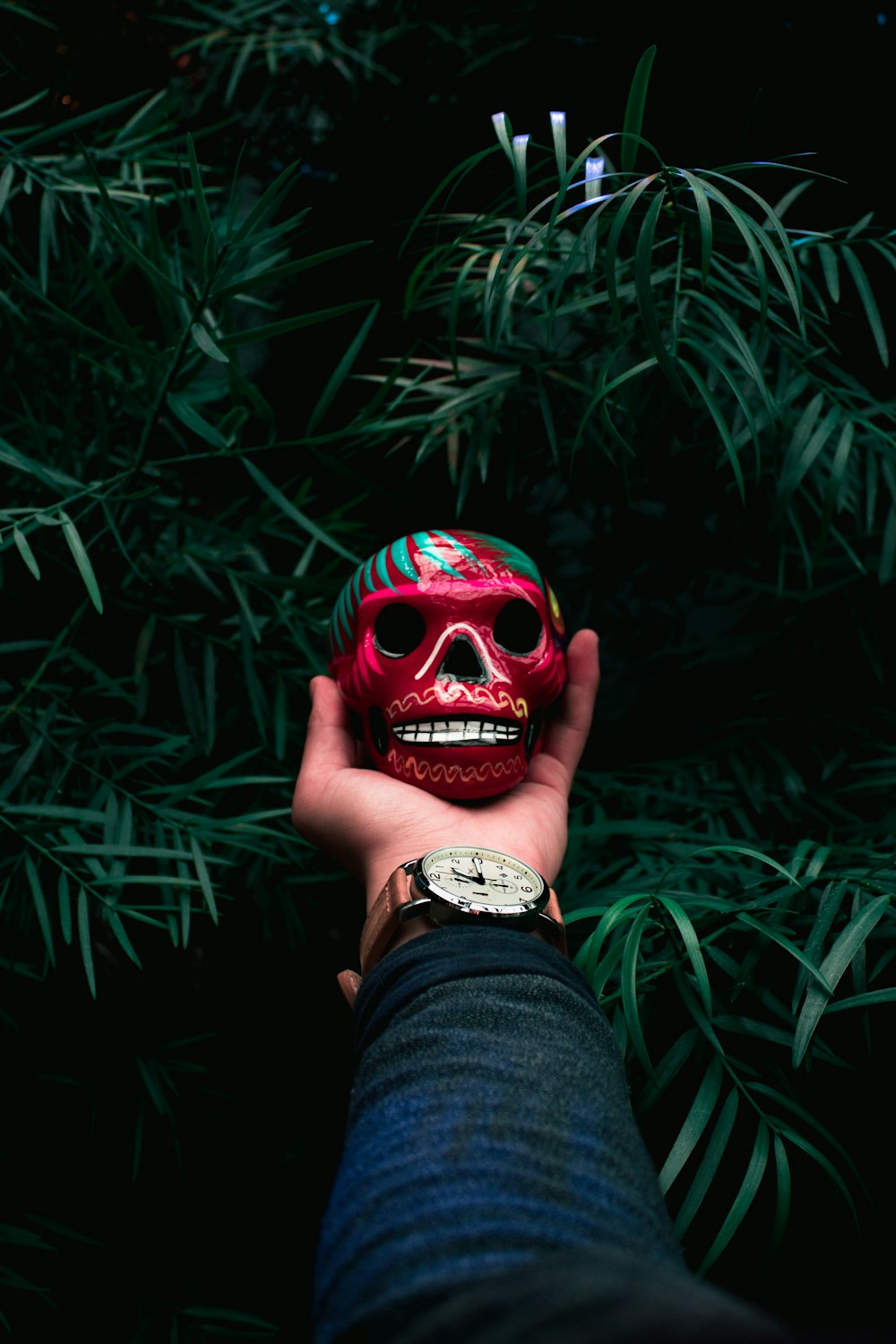 person holding red and green skull bauble