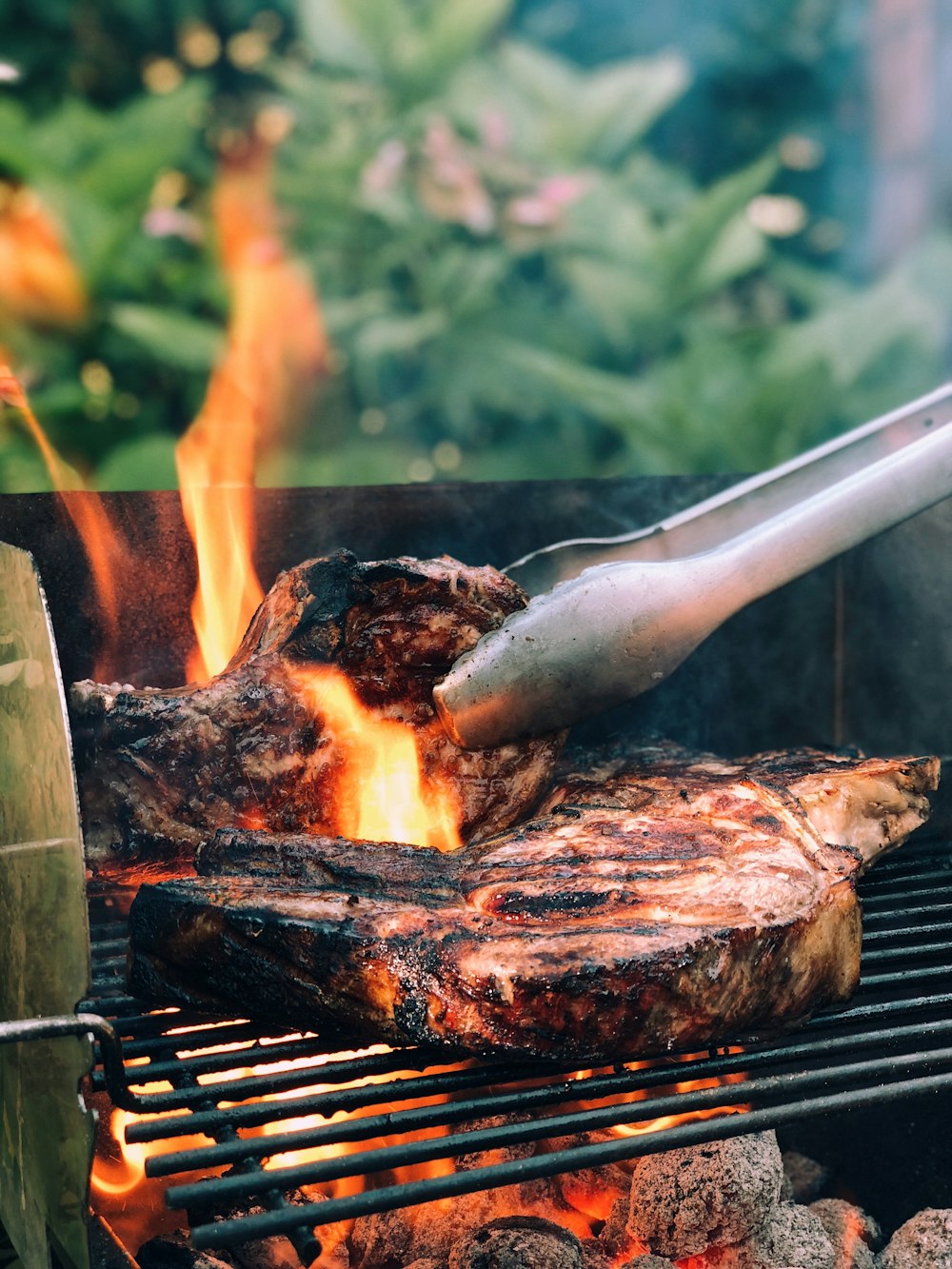 graue Metallzange und gegrilltes Fleisch mit Feuer