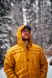men wearing orange down jacket standing on snow field near trees