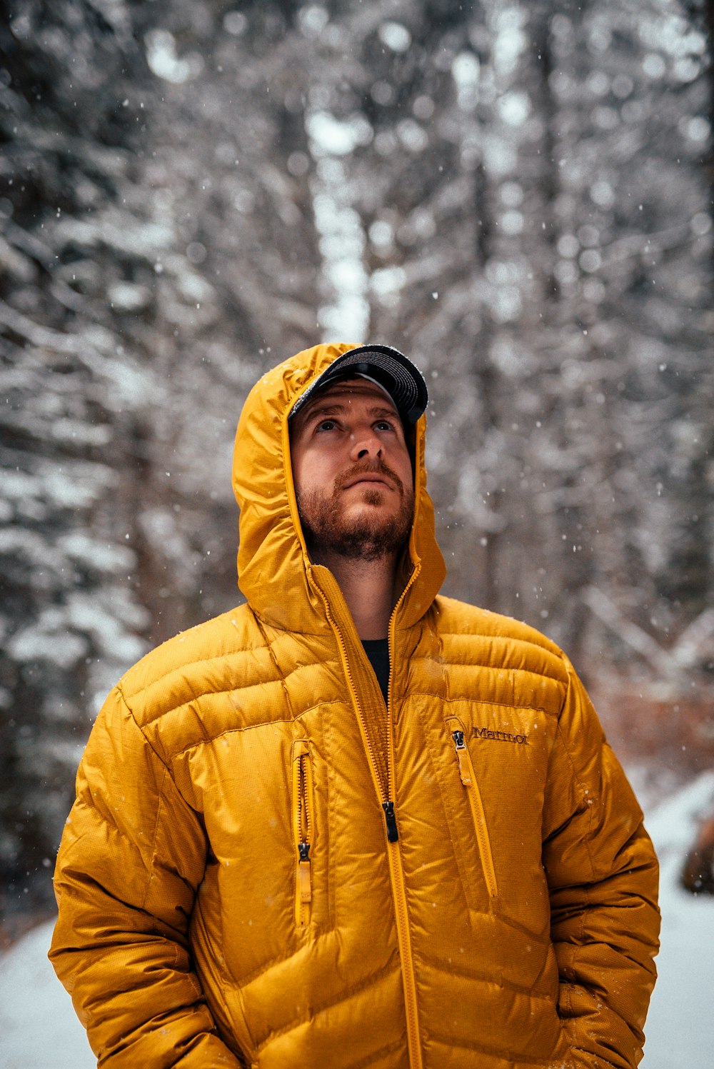 men wearing orange down jacket standing on snow field near trees