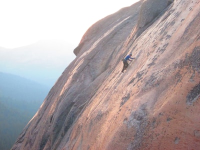 A climber scaling a steep rock face in the mountains.