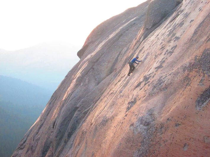 Close-up of climbing shoes gripping a rugged rock face in bright sunlight