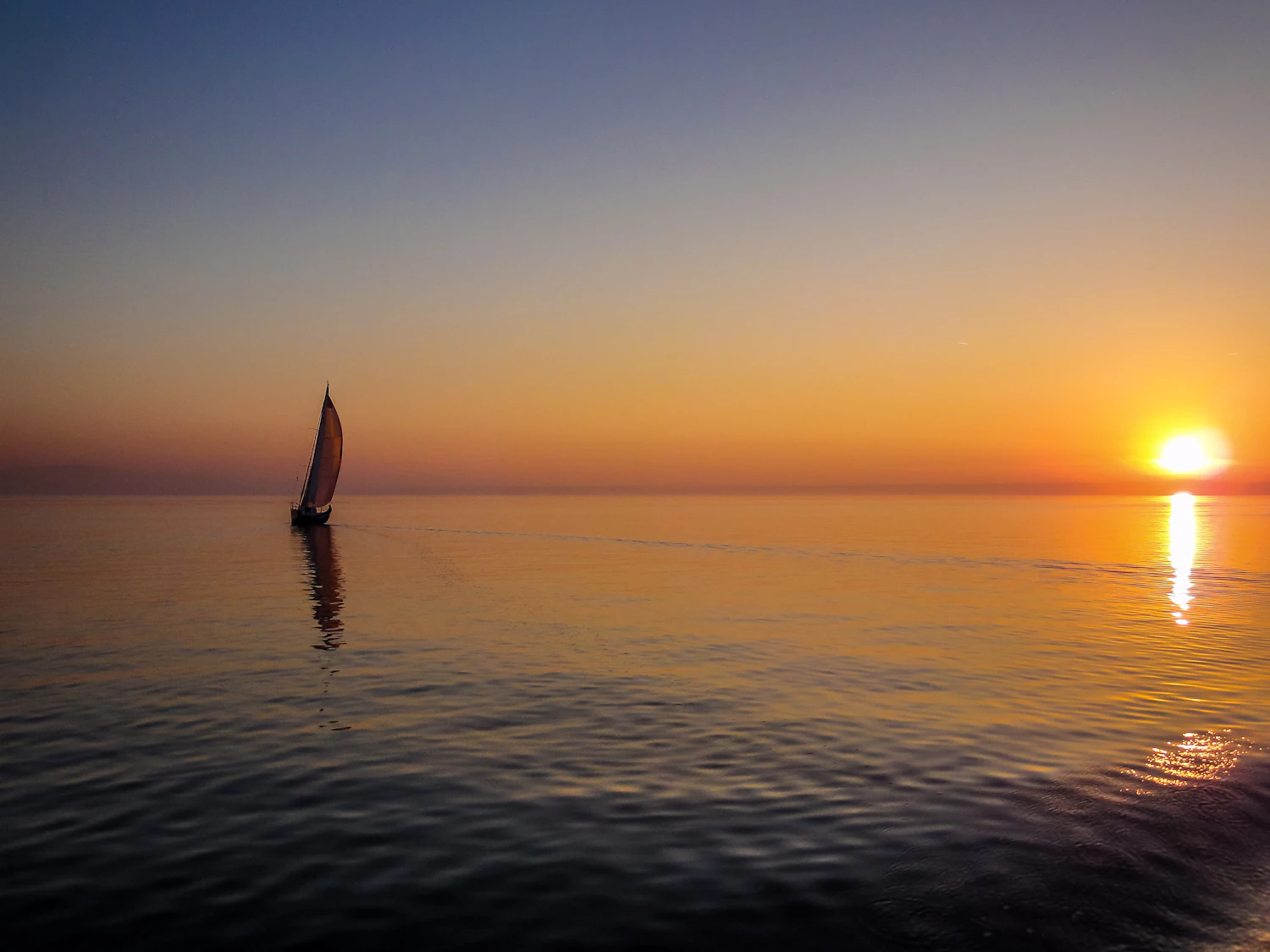 A lone sailboat on open water at dusk