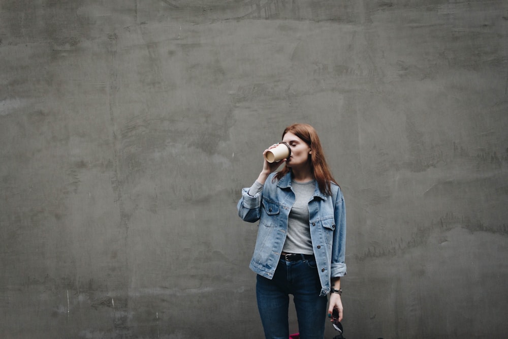 woman drinking on mug near gray wall during daytime