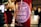 A round sticker with the text 'TTIP GAME OVER' is placed on a red pole. The background is blurred with silhouettes of people walking, indicating a nighttime setting with bright city lights.
