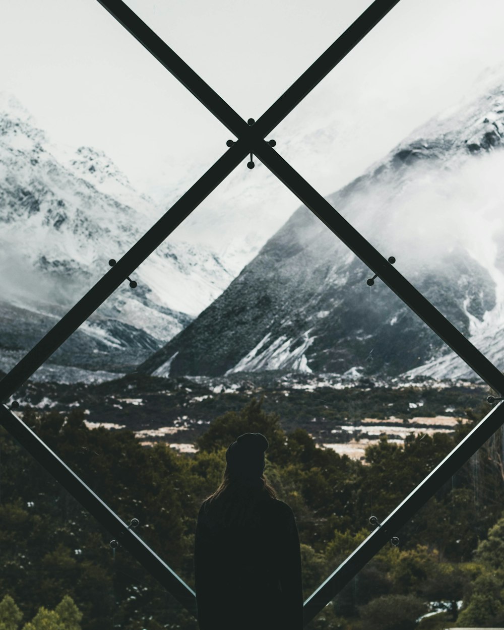 person standing on stained window looking through snow covered mountain