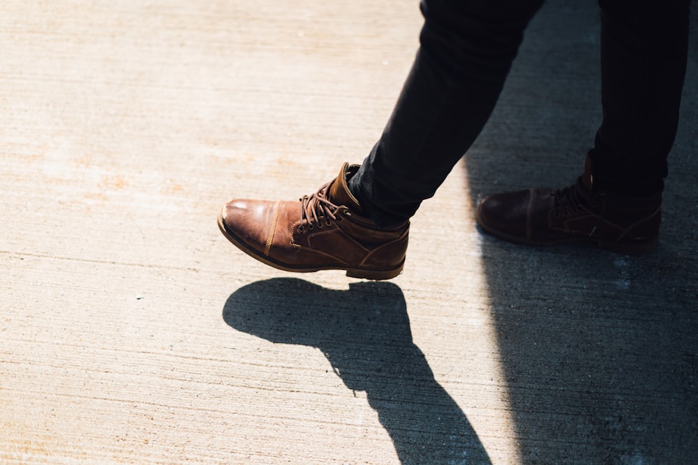 茶色の革靴を履いて昼間、灰色のコンクリートの上を歩く人