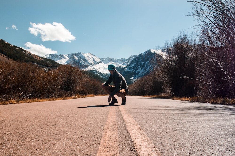 person squatting in the middle of road near snow-capped mountain at daytime