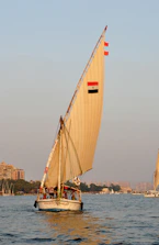 A traditional felucca boat gently gliding on the Nile at dawn with mist rising from the water.