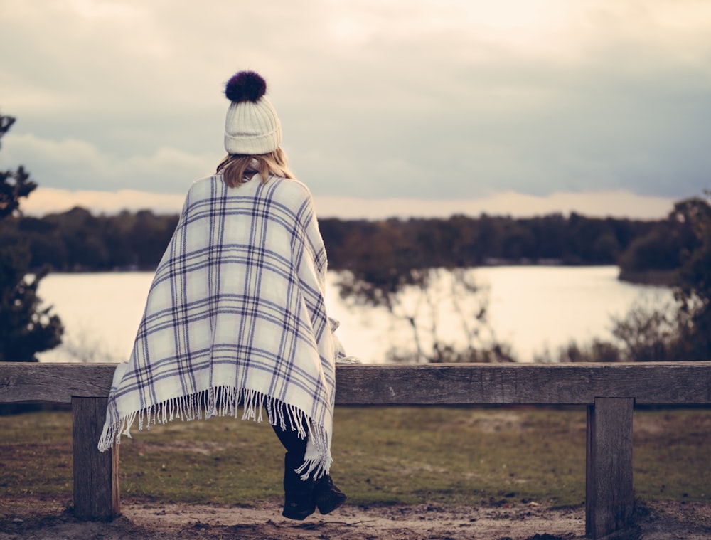 woman sitting on gray wooden bench viewing body of water