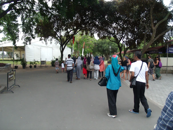 A group of participants, young and old, smiling and waving as they walk along a tree-lined path wearing green and white event shirts.