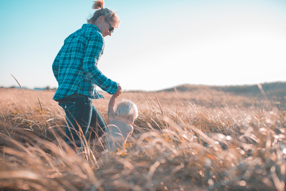 woman holding toddler waling near brown grass during daytime