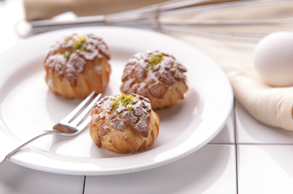 three pastries on ceramic plate with fork