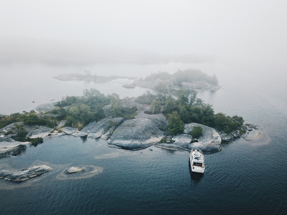 昼間の霧のある灰色と緑の島のそばにある白いヨットドックの航空写真