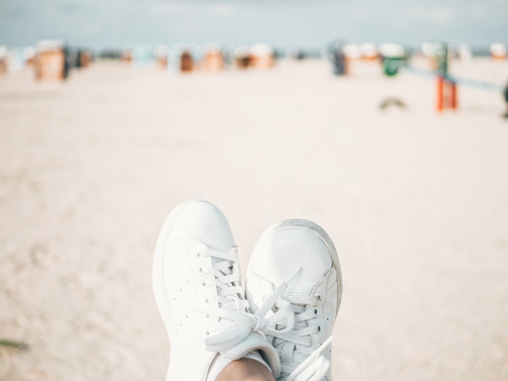 person wearing pair of white adidas low-top lace-up shoes