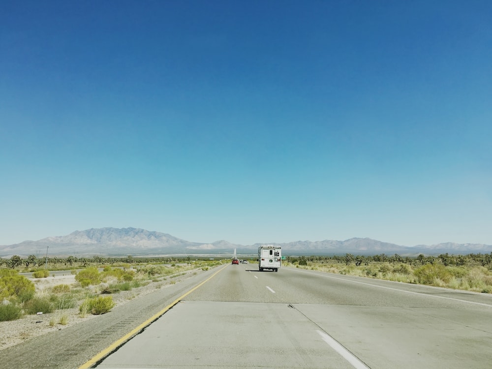 white car on gray road under blue sky photography