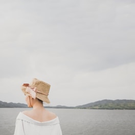 A casual weekend scene featuring a woman wearing a chic, soft-colored straw hat near the shore.