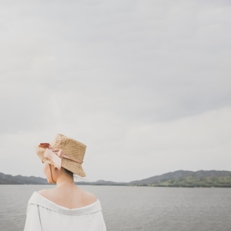 A casual weekend scene featuring a woman wearing a chic, soft-colored straw hat near the shore.