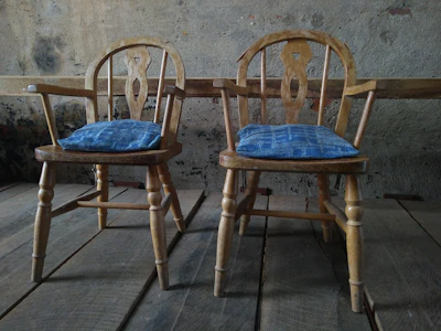 A rustic wooden dining chair with a blue cushion, set against a soft blue wall.